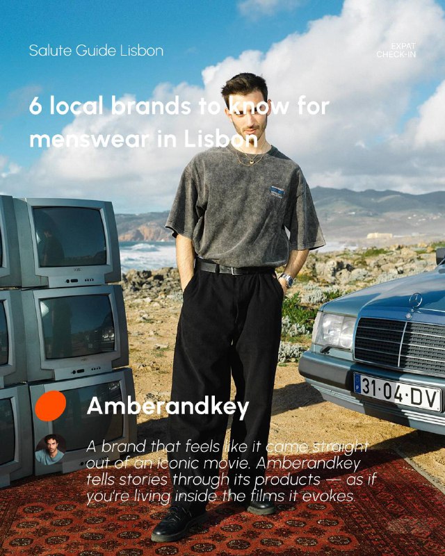 Full-body shot of a man posed outdoors beside a vintage car wearing casual trousers and a faded t-shirt, suggesting retro-inspired menswear aesthetics.