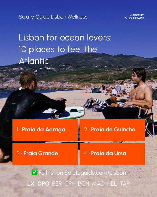 Two people sitting on a sunny Lisbon beach with surfboards, sunbathers on sand and rocky coastal hills in the background