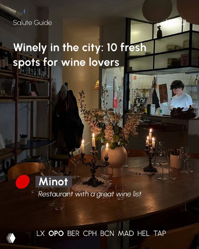 Dimly lit restaurant interior with candles on a wooden table, bottles on shelves and a person behind the bar, evoking a neighbourhood wine spot.