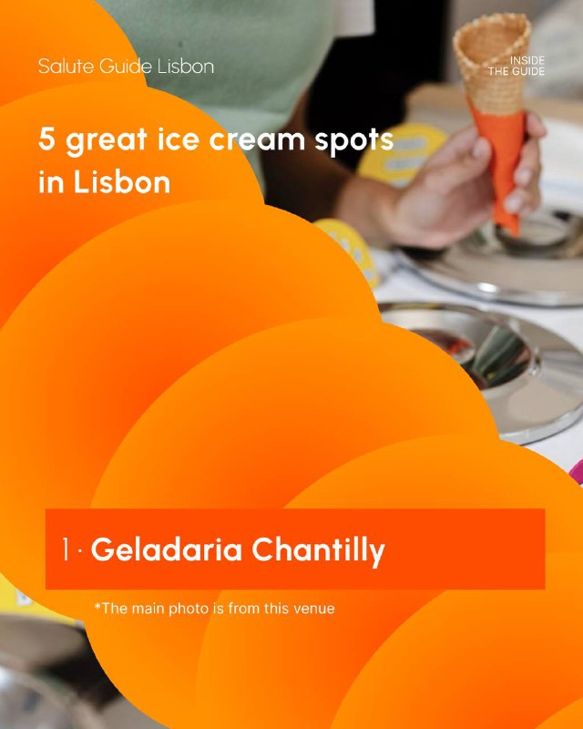 Close-up of a person holding an ice cream cone above stainless-steel gelato pans at a shop counter, with warm interior colours.