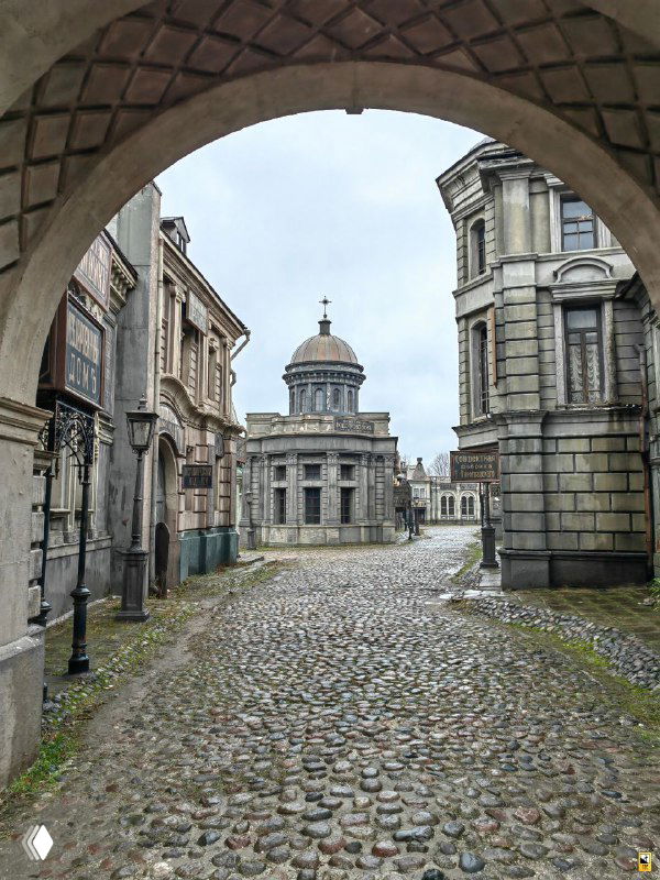 Улица с булыжной мостовой и аркой в декорациях Мосфильма: фанерные фасады, серое небо и ощущение петербургской сцены на открытом павильоне.