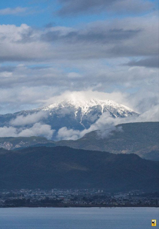 Снежная вершина горы на фоне облачного неба, вид из окрестностей Фетхие; крупная заснеженная шапка доминирует над долиной и городом внизу.
