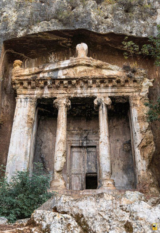 Крупный план гробницы в скале с колоннами и порталом: хорошо просматриваются каменная резьба, архаичные формы и следы времени на поверхности камня.