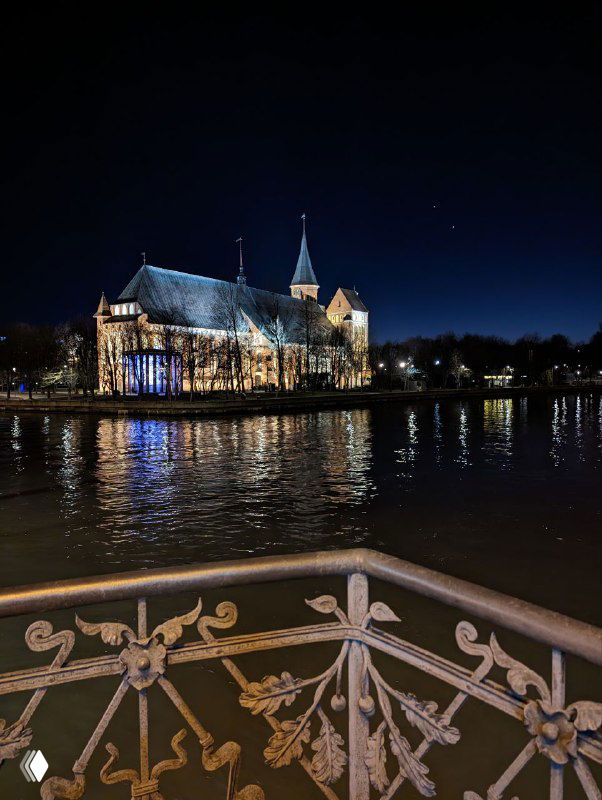 Кафедральный собор на острове Канта вечером, отражение огней в воде реке и декоративная ограждающая решетка на переднем плане.