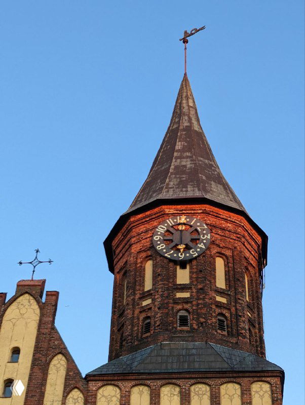 Часовая башня собора Канта крупным планом на фоне голубого неба, видна старинная кирпичная кладка и циферблат часов на башне.