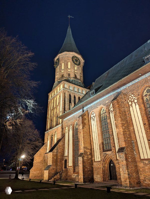 Ночной общий план собора с подсветкой и боковым ракурсом: массивные контуры, витые арки и игра света на кирпичах в темноте.