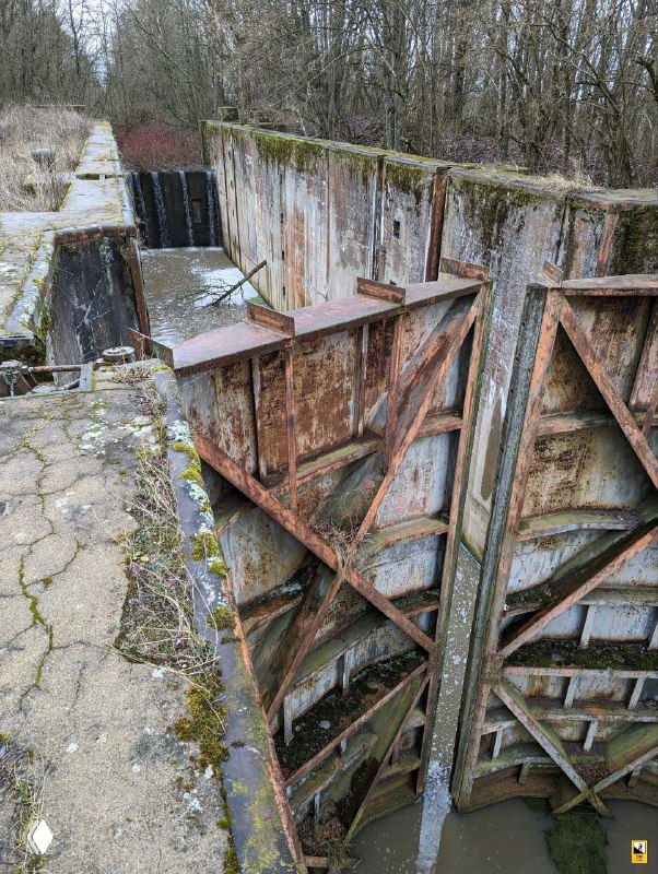 Крупный план заржавевших металлических створок шлюза №2 Мазурского канала: бетонные борта, мох и следы коррозии вокруг.