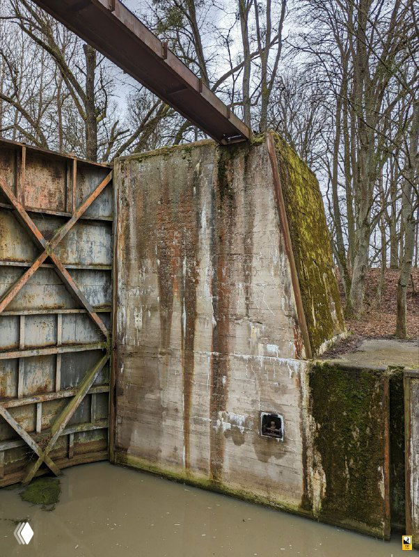 Близкий ракурс высокой бетонной стены шлюза с мхом, трещинами и ржавыми следами от металлических элементов конструкции.