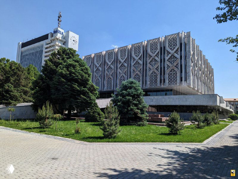 Пример советско-модернистского здания в Ташкенте с характерными декоративными элементами фасада; зелёная зона и газон на переднем плане добавляют контраста.