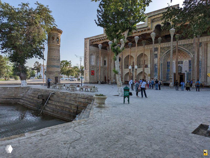 Пруд и прилегающая открытая площадь рядом с архитектурными памятниками Бухары; люди гуляют и фотографируются у исторических ансамблей.