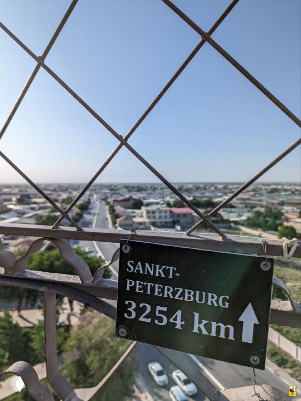 Табличка SANKT-PETERZBURG и вид через металлическую решётку со стрелкой и указанием расстояния 3254 km — панорама города.
