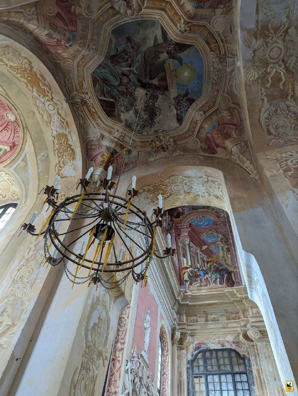 Детали потолочных фресок и люстра внутри костела: цветные библейские сюжеты, объёмные иллюзии и живописные орнаменты в барочном стиле.
