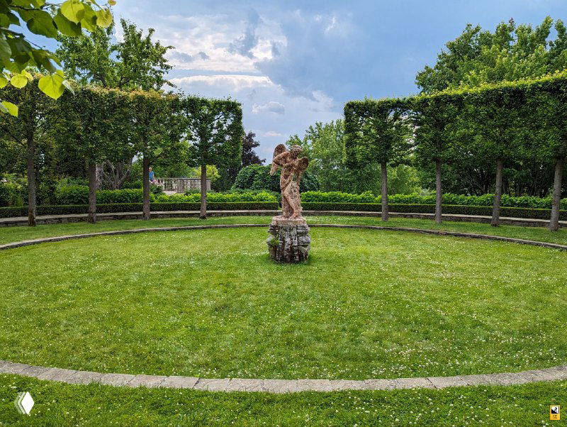 Круглая лужайка с небольшой скульптурой в центре и аккуратно подстриженными живыми стенами — архитектура европейского парка на фоне усадьбы Ореховно.