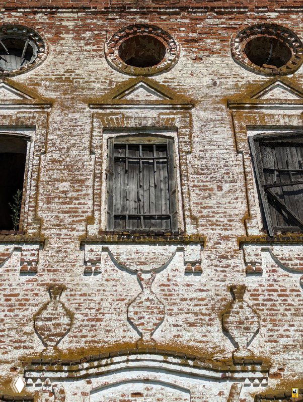 Фрагмент кирпичной стены церкви с оконными проёмами и декоративными узорами на фасаде; облупившаяся кладка и следы времени.