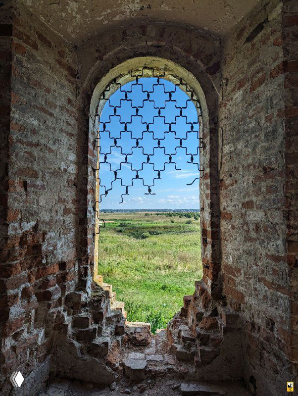 Окно с фигурной арочной решёткой в стене церкви, через которое открывается вид на суздальское ополье и дальние поля, рама без остекления.