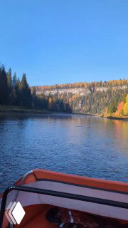 Вид с носа лодки по реке Усьва: плавный изгиб русла, спокойная поверхность воды и лесистые склоны в тёплых осенних оттенках за горизонтом.