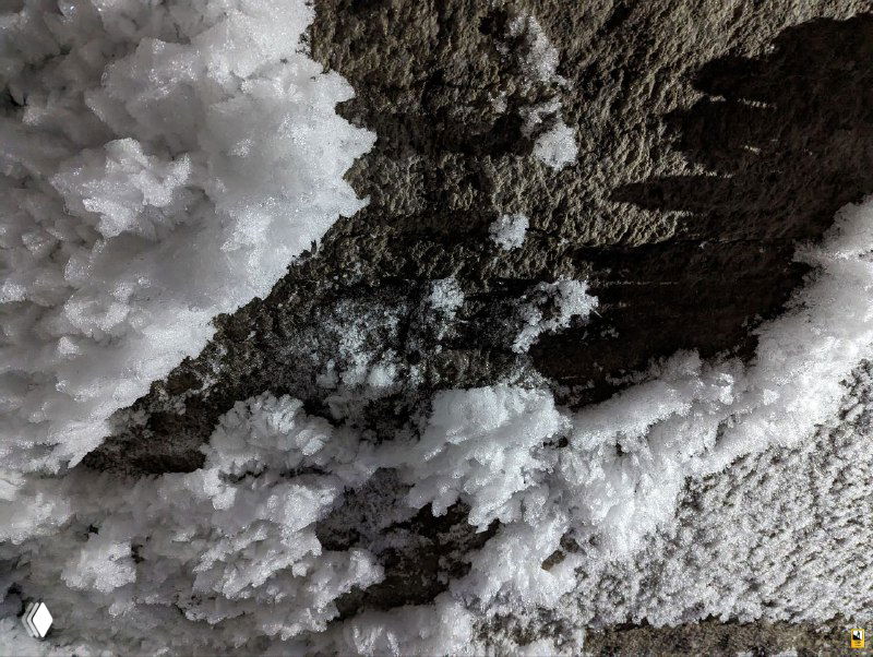 Крупный план сублимационных и натечных ледяных кристаллов на каменной поверхности внутри Кунгурской пещеры; текстура и форма видны в искусственном свете экскурсии.