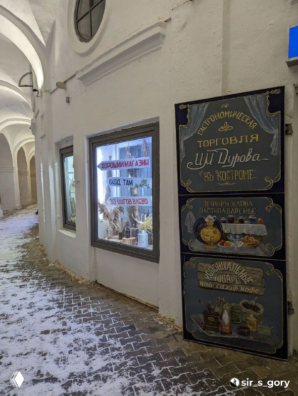 Улица с витриной магазина и табличкой в историческом проходе Красных рядов в Костроме, заснеженная тропинка рядом с витриной.