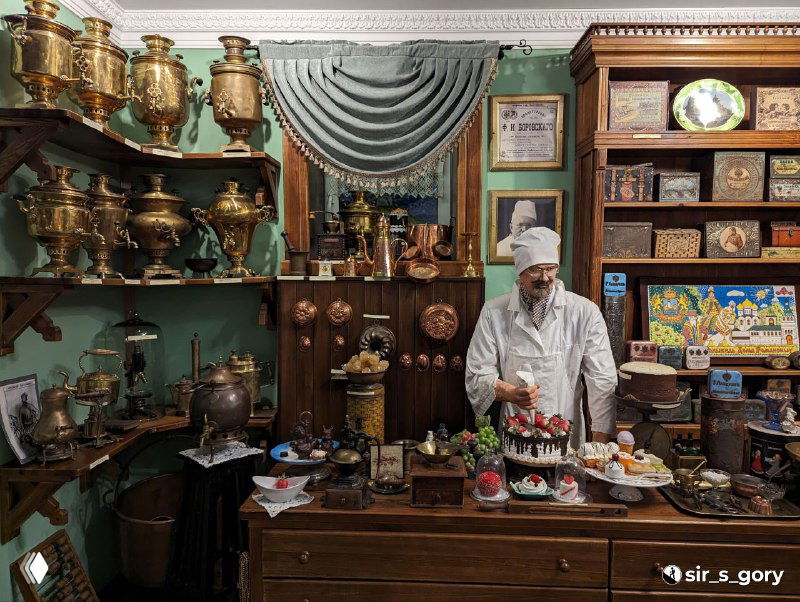 Рабочая зона в музейной лавке с мастером в белой одежде и витриной изделий — традиционные ремесленные интерьеры и посуда.