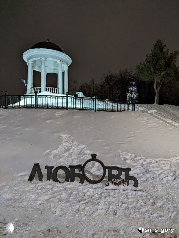 Заснеженная беседка Островского на холме вечером, белая ротонда и арт‑объект «Любовь» на переднем плане в городской зимней сцене.