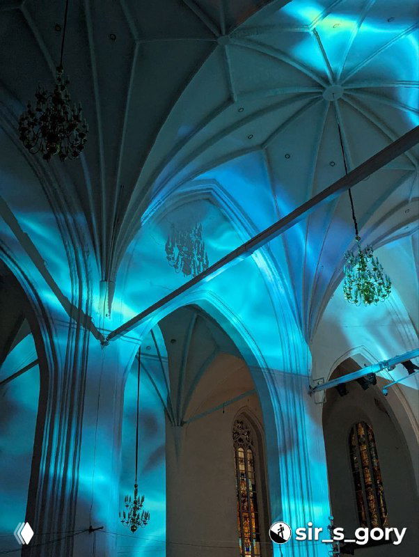 Часть потолка и арок собора, залитые голубыми и бирюзовыми прожекторами, подчёркивающими готическую архитектуру во время музыкального номера.