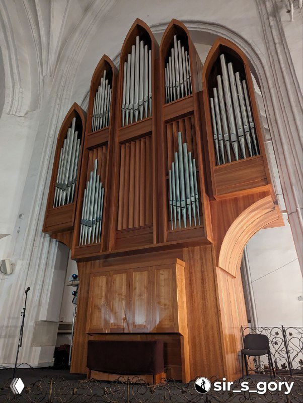 Деревянные трубы органа крупным планом: часть корпуса инструмента с деревянной отделкой и вертикальными металлическими трубами на фоне стены.