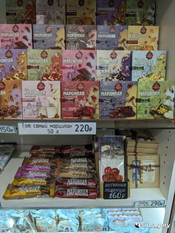 Ряды коробок и упаковок с маркированными названиями сладостей и сувениров: витрина с ассортиментом на прилавке магазина городского центра.