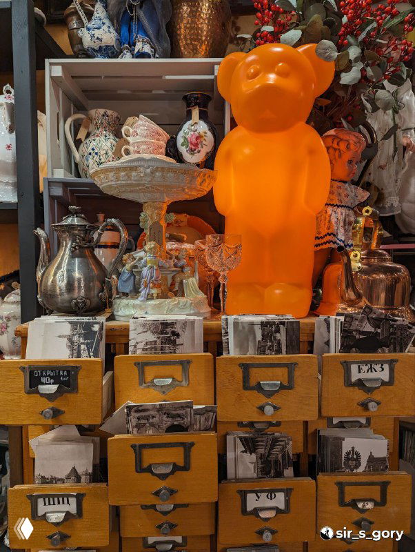 Оригинальная витрина с ярко-оранжевой фигурой в виде медведя и другими сувенирами: декоративная композиция в магазине подарков.
