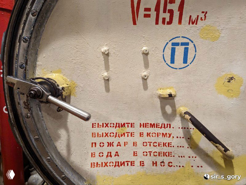 Крупный план герметичного люка подлодки с маркировкой V=151 м3 и красной предупредительной надписью на русском языке — техническая детализация экспозиции.