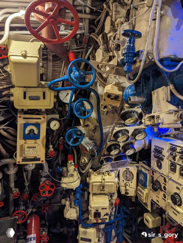 Скопление вентилей, рукояток и приборных панелей в одном из отсеков подводной лодки — демонстрация плотной механической компоновки и систем управления.
