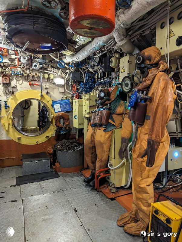 Кабина с водолазными костюмами и снаряжением на манекенах, элементы спасательного и технического оборудования на территории музейной экспозиции.