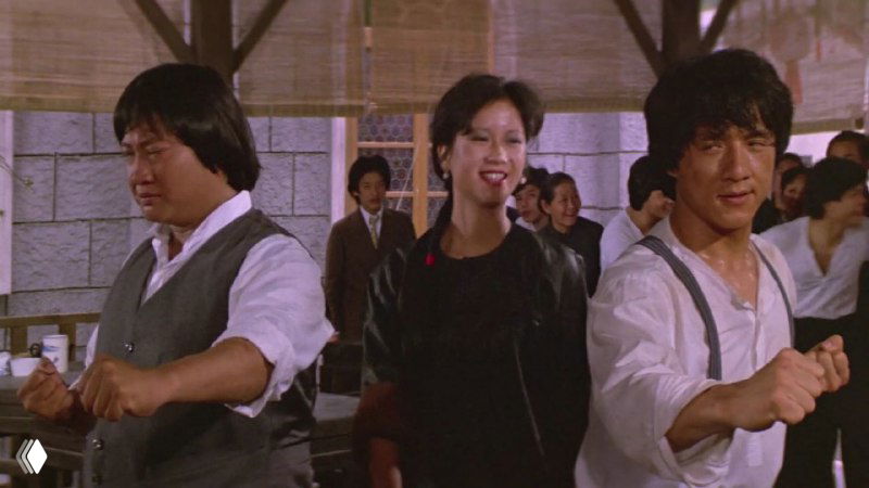 Кадр из «Проект А»: Джеки Чан и партнёрша на фоне толпы, видна репетиция акробатических и комедийных эпизодов в уличной сцене фильма.