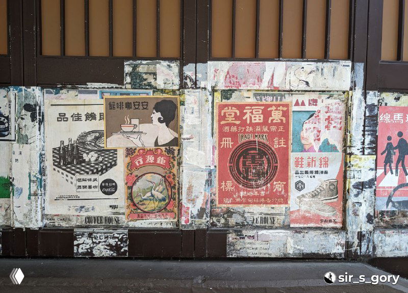 Панель с наклеенными агитационными постерами и объявлением, заметны следы времени: загрязнения, царапины и отслоившаяся бумага.