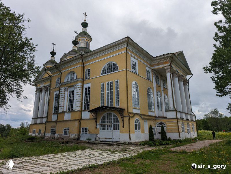 Фасад сохранившейся церкви монастыря в Тотьме с кремово‑жёлтой штукатуркой, колоннами и высоким куполом на фоне облачного неба.