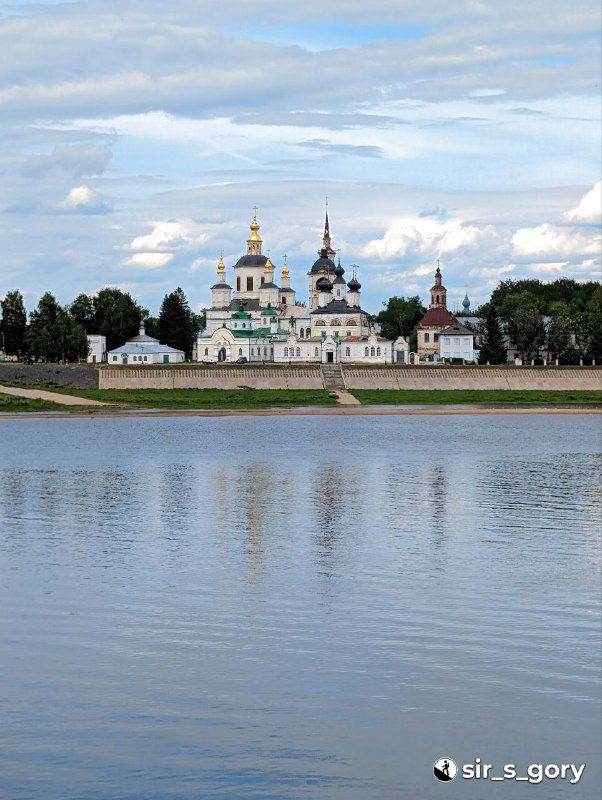 Панорамный вид через реку на архитектурный ансамбль с куполами и колокольнями, спокойная поверхность Сухоны и облачное небо, летний пейзаж.