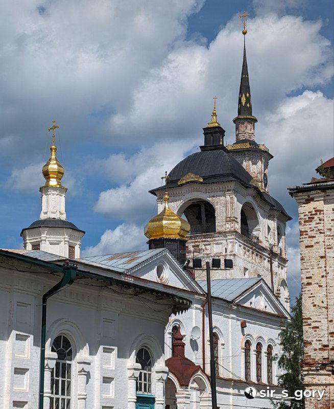 Крупный план церковной башни и золотых куполов на фоне синего неба с облаками; архитектурные детали реставрированной Николо-Гостунской церкви.