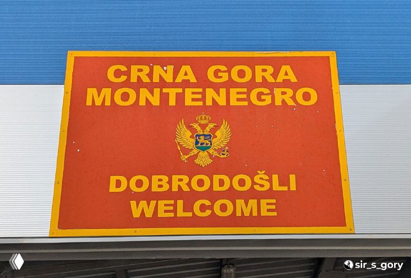 Красная приветственная табличка «Crna Gora / Montenegro — Dobrodošli / Welcome» с гербом Черногории, снятая у въезда или туристического пункта.