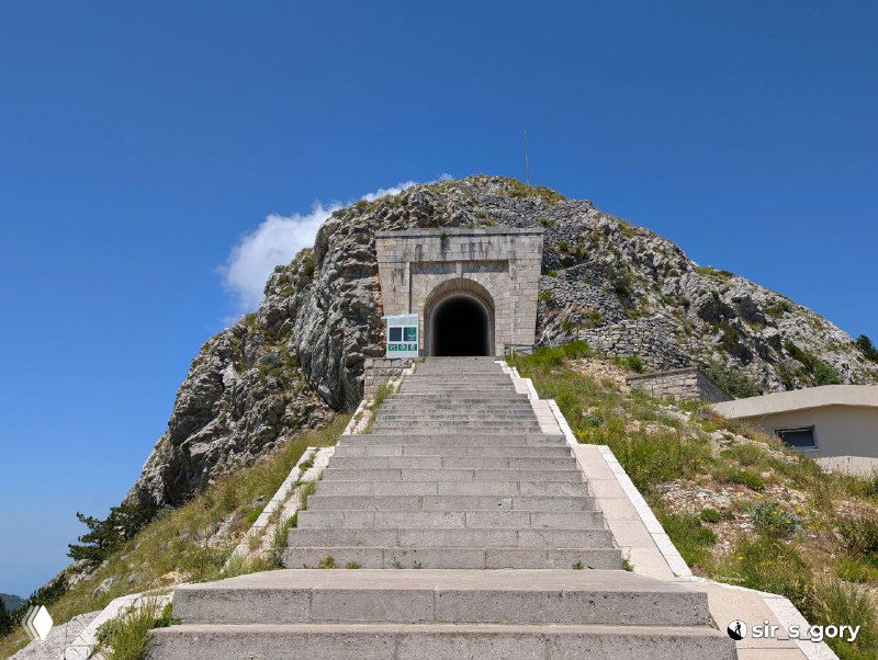 Каменные ступени и вход в мавзолей Петра Петровича Негоша на склоне Ловчена — архитектурный акцент на фоне скалы и неба.