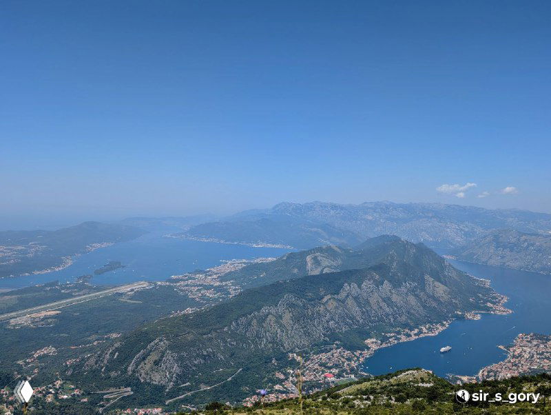 Широкая панорама Которского залива со скалистыми выступами и прибрежными селениями, вид сверху с чистой обзорностью до моря.