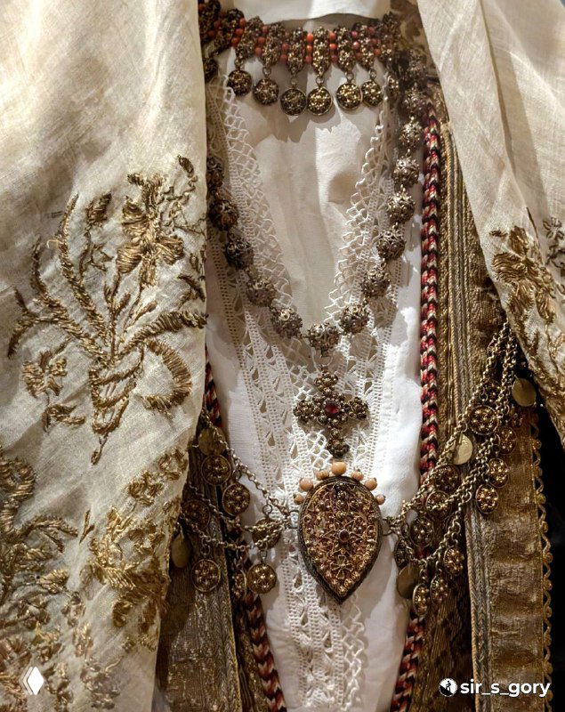 Детальный кадр традиционной черногорской вышитой одежды и ожерелья с металлическими подвесками на музейном манекене в экспозиции.