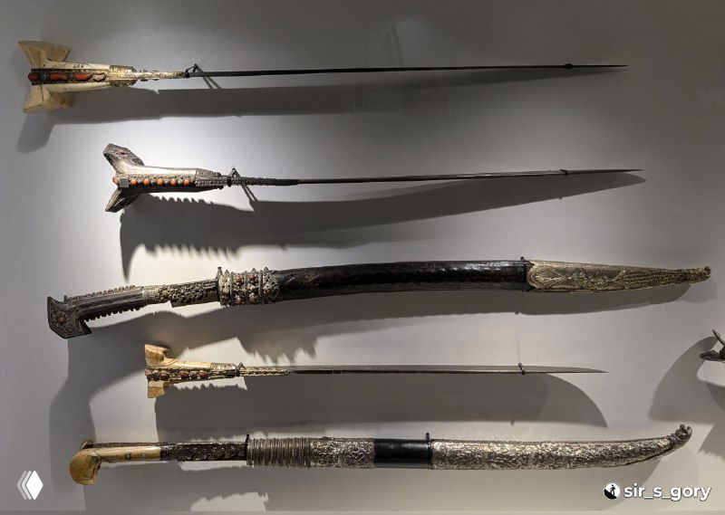 Коллекция мечей и сабель с богато украшенными эфесами и ножнами на стенде музея, демонстрирующая военную историю региона.