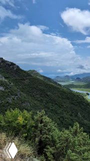 Вертикальный кадр горного склона и плёса озера: хвойные деревья в переднем плане и лёсный склон, уходящий в воду.