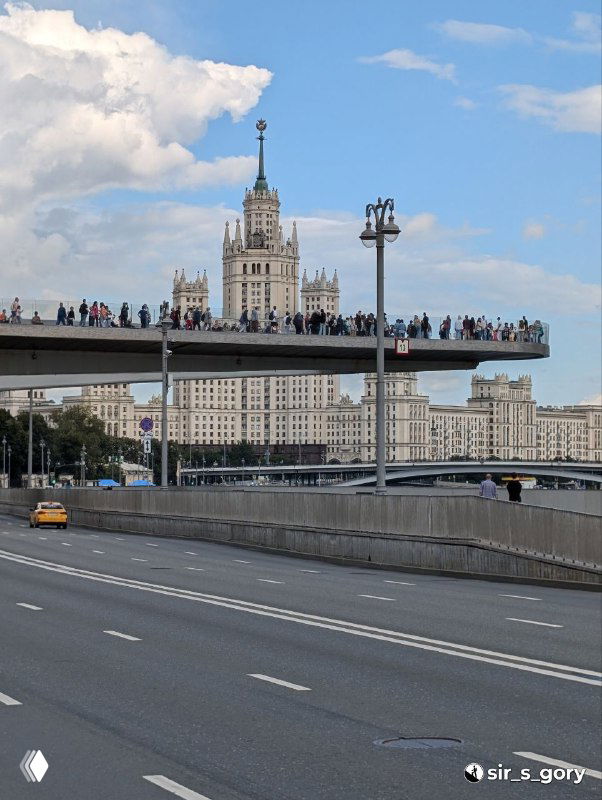 Парящий мост в Зарядье с множеством людей на смотровой площадке и высотным зданием на заднем плане — зрелищный городской пейзаж