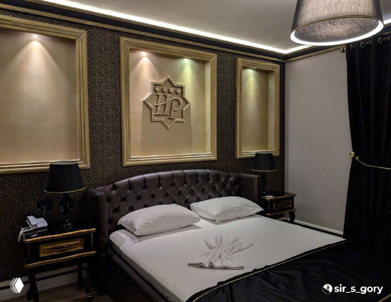 Интерьер номера отеля Hymeti's Palace: двуспальная кровать, тёмные текстуры и декоративный герб на стене, классическая отделка и лампы.