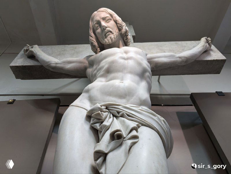 Вид снизу на торс и драпировку мраморного распятия Жан‑Жака Прадье, подчёркнутая анатомическая детализация и музейное освещение.