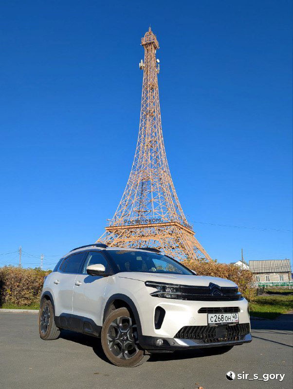 Копия Эйфелевой башни в селе Париж на фоне ясного неба и припаркованного внедорожника — местная туристическая достопримечательность и вышка связи.