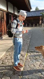 Человек с рюкзаком на мощёной улице взаимодействует с собакой в японском историческом месте — живой кадр из путешествия без указания личности.