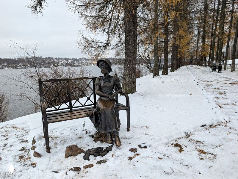 Скульптура «Дачница» у набережной Музея пейзажа: фигура женщины на скамье, заснеженная тропинка, река и осенние деревья.