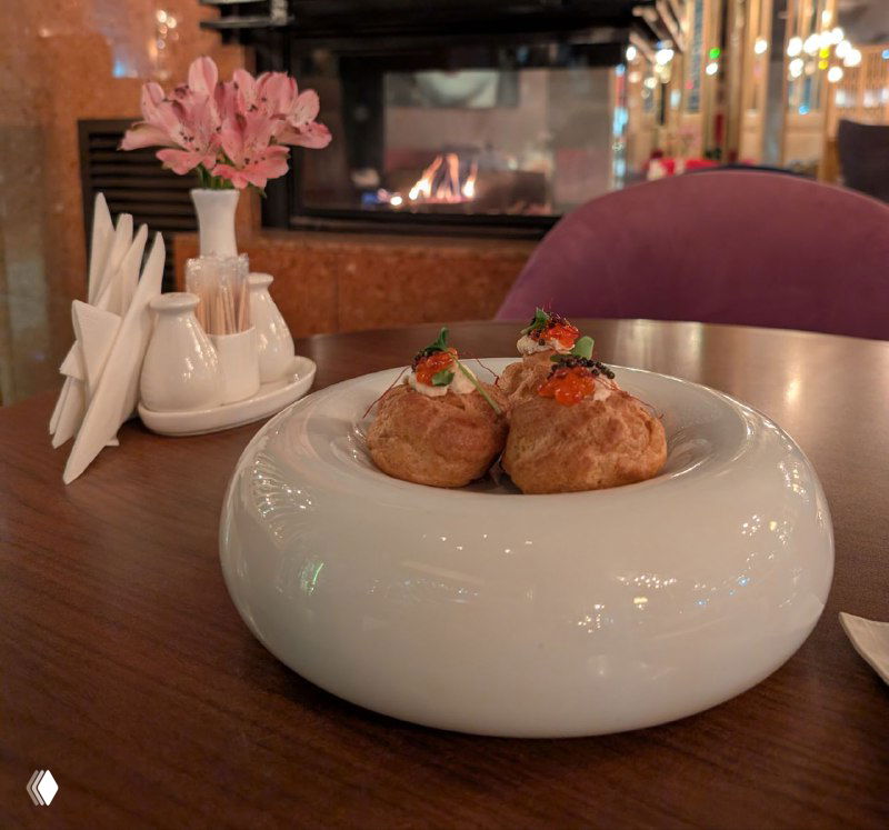 Тарелка с тёплой закуской на столе в ресторане: на заднем плане горит камин, видна сервировка и уютная зимняя атмосфера заведения.