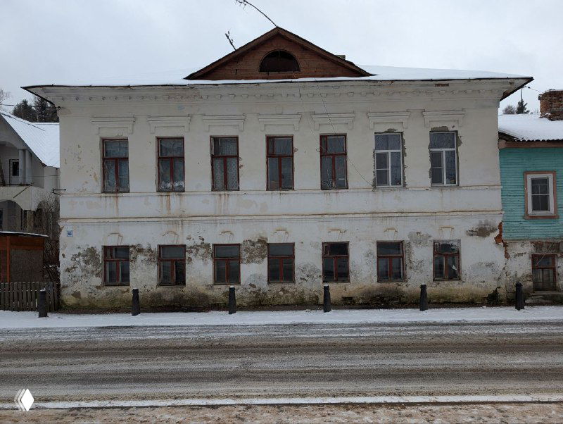 Белый двухэтажный особняк с обветшалым фасадом и заснеженной улицей перед ним — образец купеческой застройки Плёса.